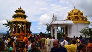 ಉಗಾಂಡದ ಸಪ್ತಗಿರಿ ಶ್ರೀ ವೆಂಕಟೇಶ್ವರ ದೇವಸ್ಥಾನದ ಆವರಣದಲ್ಲಿ ನಡೆಯುತ್ತಿರುವ ರಥೋತ್ಸವದ ದೃಶ್ಯ. ಭಕ್ತರು ಸಂಭ್ರಮದಿಂದ ರಥ ಎಳೆಯುತ್ತಿರುವುದು ಮತ್ತು ಹಿನ್ನೆಲೆಯಲ್ಲಿ ಸುಂದರವಾದ ಚಿನ್ನದ ಬಣ್ಣದ ಗೋಪುರ.