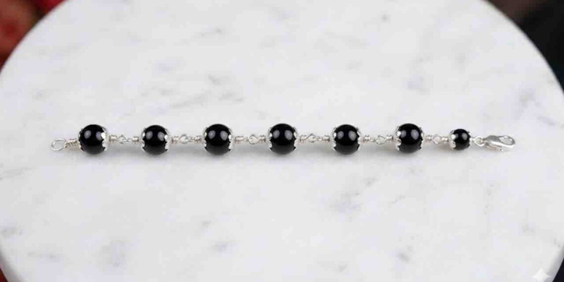 professional wide-angle HD shot of a black onyx bead bracelet with ornate silver caps laid horizontally on a white marble surface.