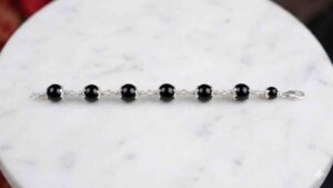 professional wide-angle HD shot of a black onyx bead bracelet with ornate silver caps laid horizontally on a white marble surface.