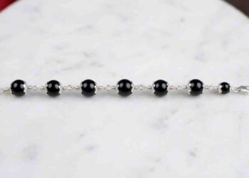 professional wide-angle HD shot of a black onyx bead bracelet with ornate silver caps laid horizontally on a white marble surface.
