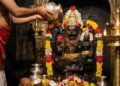 Divine AI-generated image of Lord Narasimha Swami idol being bathed with honey (Abhisheka) by a priest in a traditional temple setting with oil lamps and flowers.