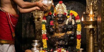 Divine AI-generated image of Lord Narasimha Swami idol being bathed with honey (Abhisheka) by a priest in a traditional temple setting with oil lamps and flowers.