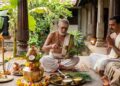 A traditional Hindu ritual scene featuring a priest performing Punyahavachana with Panchagavya, a decorated kalasha, and a holy cow in a traditional South Indian courtyard.