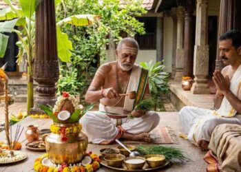 A traditional Hindu ritual scene featuring a priest performing Punyahavachana with Panchagavya, a decorated kalasha, and a holy cow in a traditional South Indian courtyard.