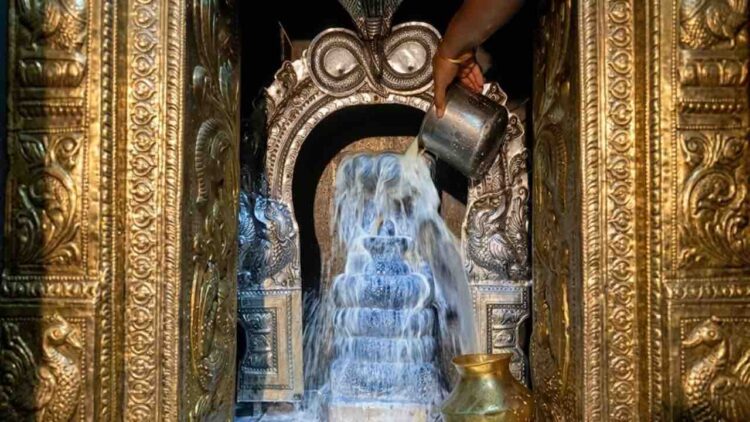 Close-up photograph of a milk abhishekam being performed on a Shiva Lingam at Thirupampuram Seshapureeswarar Temple, showing a hand pouring milk.