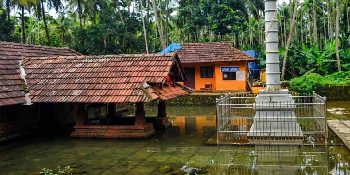 Arakkuparamba Ardhanariswara Temple in Malappuram Kerala featuring the main sanctum and stone flagstaff surrounded by water.