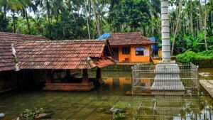 Arakkuparamba Ardhanariswara Temple in Malappuram Kerala featuring the main sanctum and stone flagstaff surrounded by water.