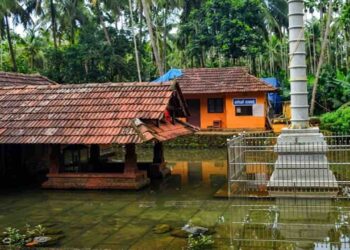 Arakkuparamba Ardhanariswara Temple in Malappuram Kerala featuring the main sanctum and stone flagstaff surrounded by water.