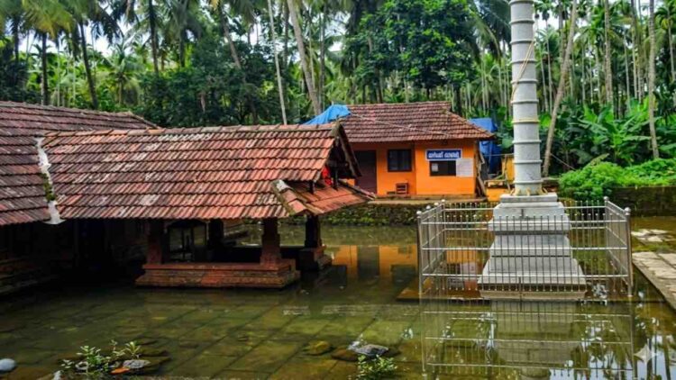 Arakkuparamba Ardhanariswara Temple in Malappuram Kerala featuring the main sanctum and stone flagstaff surrounded by water.
