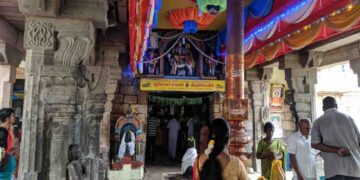 Interior of Bhoominathaswamy Temple in Mannachanallur showing carved stone pillars, a golden flagstaff (Dhvajastambha), and devotees praying near the sanctum.