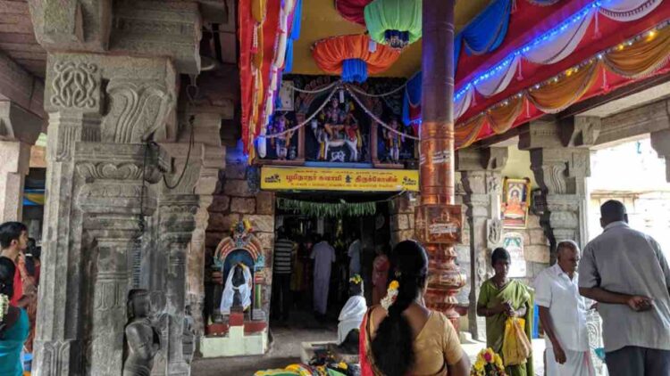 Interior of Bhoominathaswamy Temple in Mannachanallur showing carved stone pillars, a golden flagstaff (Dhvajastambha), and devotees praying near the sanctum.