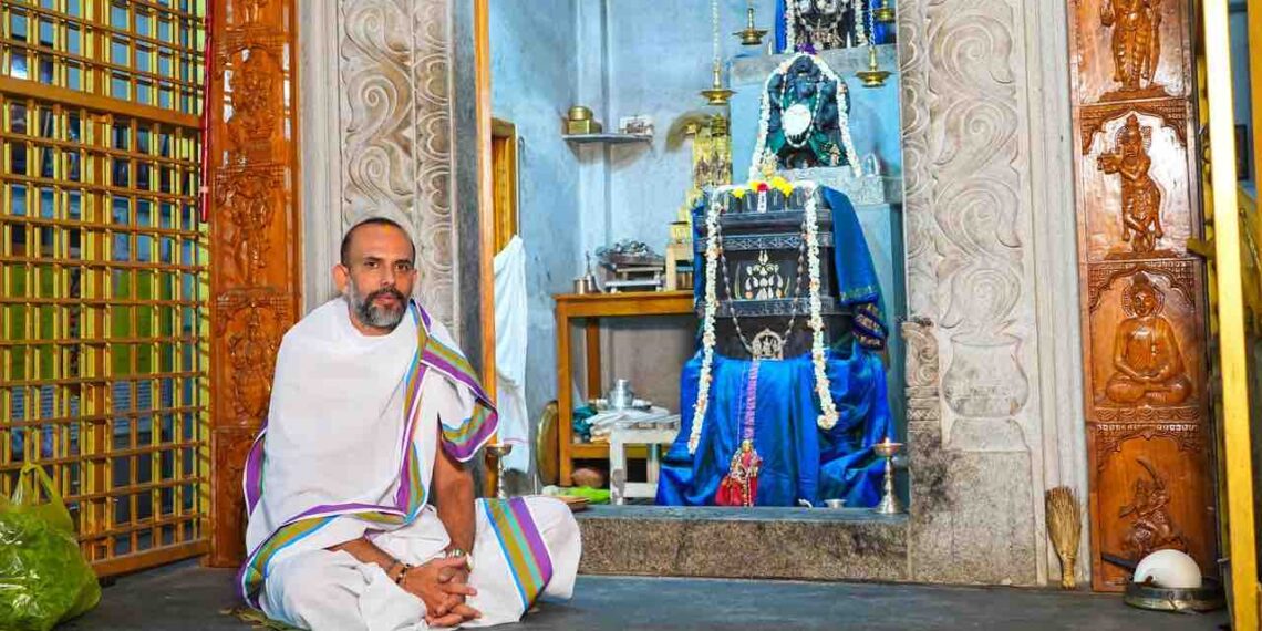 Spiritual thinker Manjunath Bharadwaj sitting in a traditional attire in front of a Hindu deity sanctum.