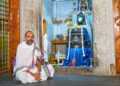 Spiritual thinker Manjunath Bharadwaj sitting in a traditional attire in front of a Hindu deity sanctum.