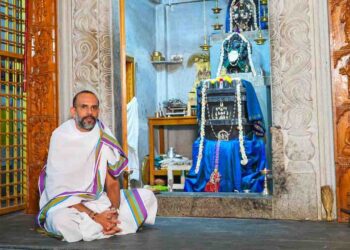 Spiritual thinker Manjunath Bharadwaj sitting in a traditional attire in front of a Hindu deity sanctum.