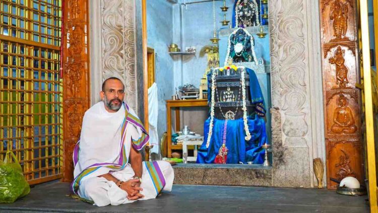 Spiritual thinker Manjunath Bharadwaj sitting in a traditional attire in front of a Hindu deity sanctum.