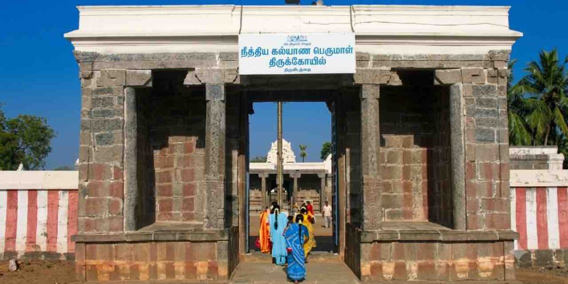 Main entrance gateway of the historic Nithya Kalyana Perumal Temple in Thiruvedanthai, Tamil Nadu, with devotees entering and a clear blue sky.