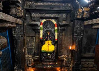 Sanctum of Sri Suddha Ratneswarar Temple at Oottathur, Tamil Nadu, featuring the sacred deity amidst ancient stone architecture and oil lamps.