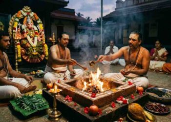 A realistic image of a Varahi Homam (sacrificial fire ritual) being performed. Priests are seated around a square fire pit (Homa Kunda), offering materials into the flames. In the background, there is a decorated idol of Goddess Varahi (with a boar face) and devotees seated. Various ritual items like coconuts, pomegranates, and dried red chilies are visible in the foreground.