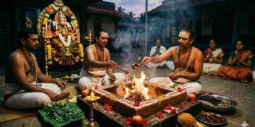 A realistic image of a Varahi Homam (sacrificial fire ritual) being performed. Priests are seated around a square fire pit (Homa Kunda), offering materials into the flames. In the background, there is a decorated idol of Goddess Varahi (with a boar face) and devotees seated. Various ritual items like coconuts, pomegranates, and dried red chilies are visible in the foreground.