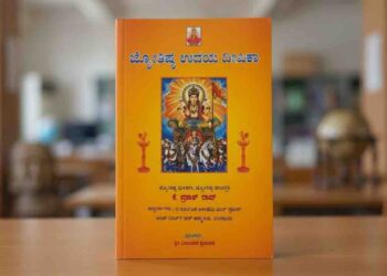 ⁠A close-up photograph of the vibrant orange cover of a Kannada astrology book titled 'Jyotishya Udaya Deepika' by K. Prakash Rao. The cover features a central illustration of Lord Surya in a seven-horse chariot, flanked by oil lamps, with details of the author's title and the publisher at the bottom. The book stands vertically on a wooden desk with a blurred library background.