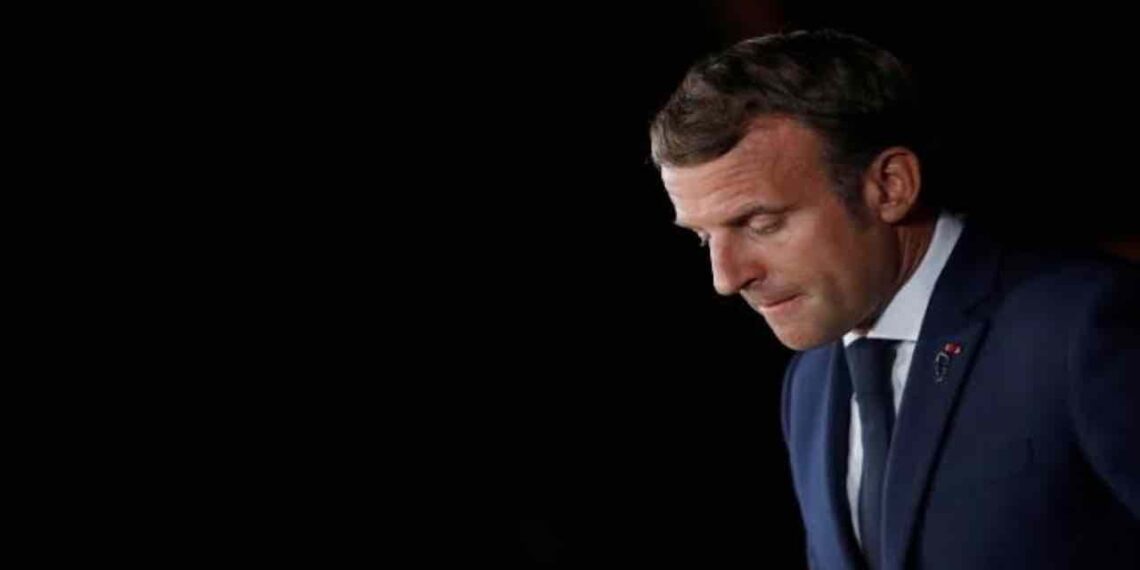 A pensive profile of French President Emmanuel Macron against a black background.