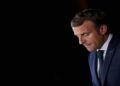A pensive profile of French President Emmanuel Macron against a black background.