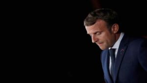 A pensive profile of French President Emmanuel Macron against a black background.